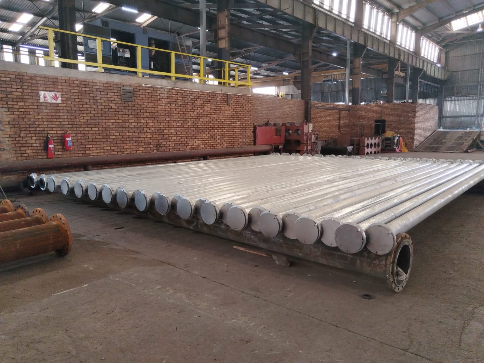 Long galvanized steel pipes with end caps staged on the Wetpipe fabrication floor