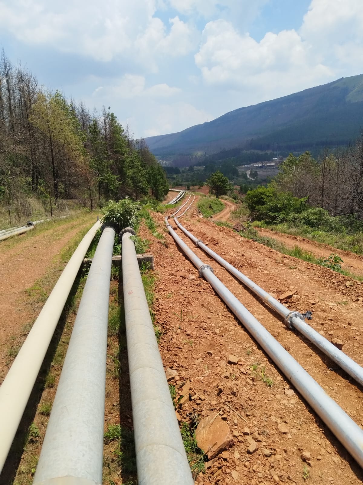 Multiple overland slurry pipelines running down a valley toward a mining plant